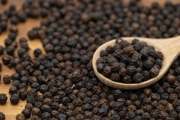 Dry heap black pepper isolated on wooden chopper board with wooden spoon