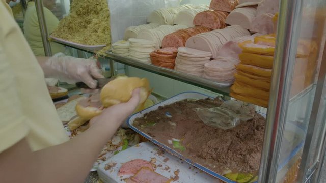 A closeup top view shot of a local vendor putting different types of meat in bread to make a sandwich inside its snack stand.