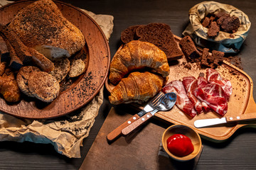 Croissant and Brown bread in wooden dish on table in the dark grunge style.