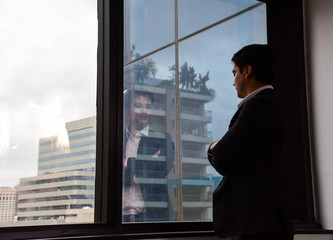 Fototapeta premium A handsome businessman look out of his office window on the tall building and think about the company development and new project in the future/Vision/Business going forward