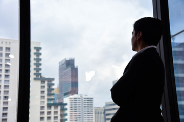 Fototapeta na wymiar A handsome businessman look out of his office window on the tall building and think about the company development and new project in the future/Vision/Business going forward