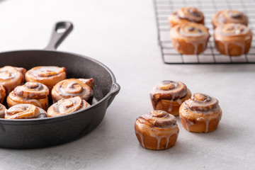 Homemade baked cinnamon rolls baked in an iron skillet cooling on cooling rack with icing