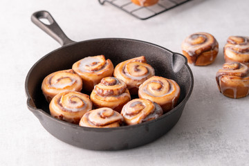 Homemade baked cinnamon rolls baked in an iron skillet cooling on cooling rack with icing