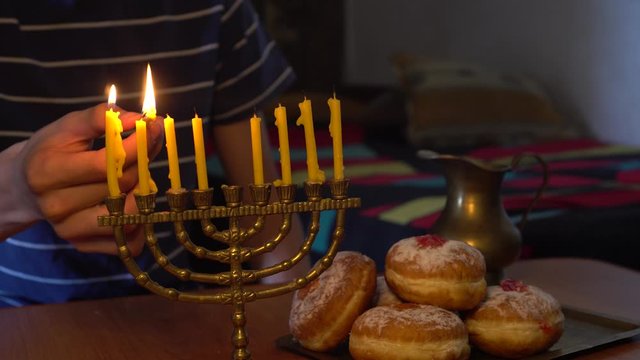 Man Lights the Hanukkah Menorah at home, with family and friends. Jewish festival. Kosher Dessert  Doughnuts - Sufganiyot