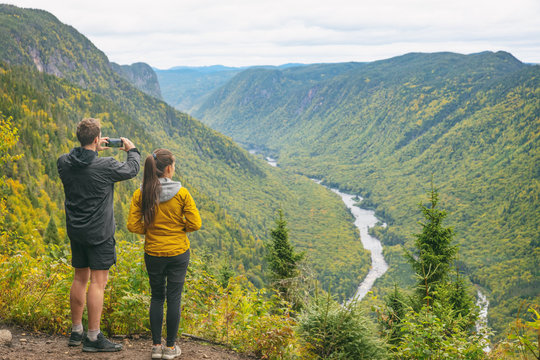 Nature trek hike couple tourists people taking pictures with phone at view of mountain landscape in Autumn forest Canada travel, Jacques Cartier National Park, boreal forest background.