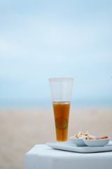 A tall glass of cold iced tea with sliced lemons on the beach with seascape background