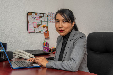 empresaria latina morena, mujer milenial, en oficia bufete sonriente con telefono celular