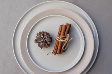 Plates for Christmas dinner on table decorated with pine cone and cinnamon sticks. Minimalism style. Beautiful festive table setting. Xmas and New Year traditions in winter hoidays.