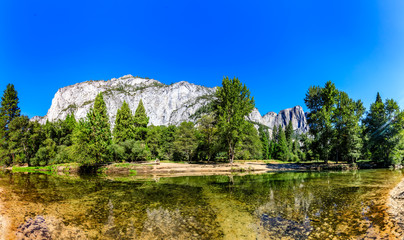 Fototapeta na wymiar The clean flat Merced river reflects trees in the foreground and the tall granite of Eagle Peak in Yosemite National Park