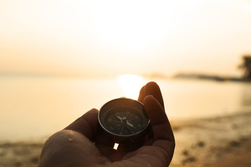 Hand holding compass on the beach.
