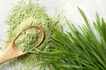 Spoon with wheat grass powder and sprouts on grey table, flat lay