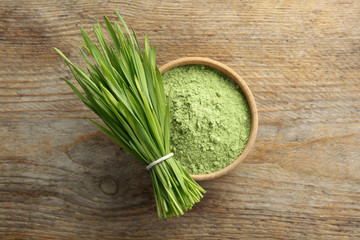 Bowl of wheat grass powder and green sprouts on wooden table, flat lay