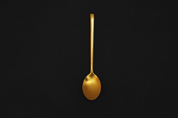 Gold spoon on black background, top view