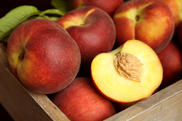 Fototapeta na wymiar Tasty peaches and leaves in wooden crate, closeup