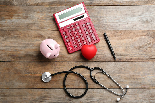Flat lay composition with calculator and stethoscope on wooden background. Health insurance concept