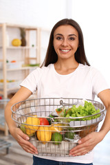 Young woman with shopping basket full of products in grocery store