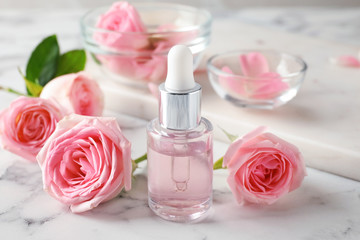 Bottle with rose essential oil and flowers on marble table