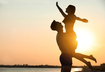 Young woman in bikini spending time with her boyfriend on beach at sunset. Lovely couple