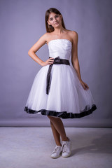 Naklejka premium Young beautiful female model in white dress on gray background. Beautiful girl in an airy dress.