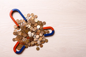 Magnets attracting coins on light wooden background, flat lay. Space for text