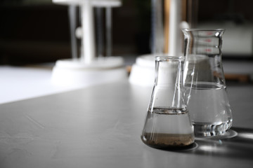 Glassware with soil extract and water on grey table, space for text. Laboratory research
