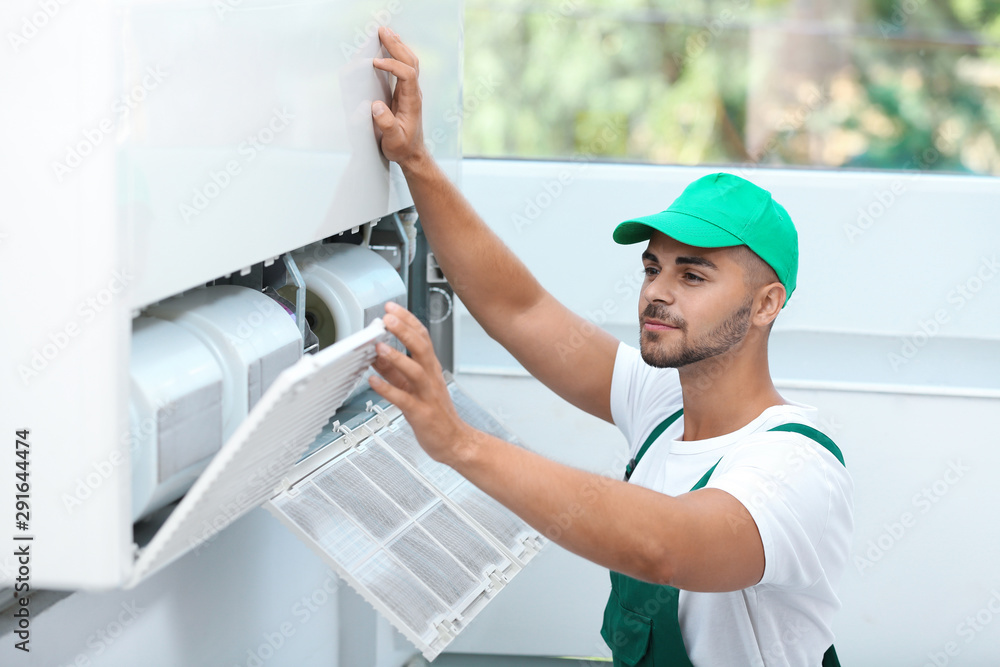 Sticker professional technician maintaining modern air conditioner indoors