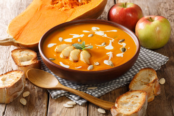 Serving of pumpkin and apple soup with seeds close-up in a bowl served with bread. horizontal