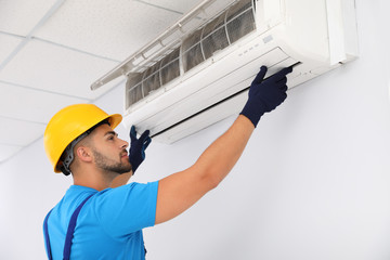 Professional technician maintaining modern air conditioner indoors