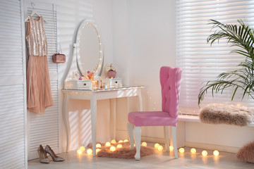 Elegant dressing table with lights and pink chair in stylish room interior