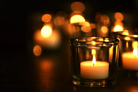 Burning candle on table against blurred background, space for text. Funeral symbol