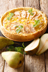 Freshly baked fruit pear tart with almonds and mint closeup on a slate board on a table. vertical