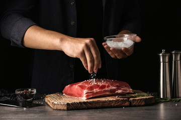 Man salting fresh raw meat on table against dark background, closeup