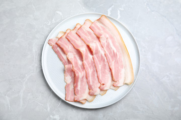 Plate of sliced raw bacon on light grey marble table, top view