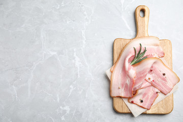 Wooden board with sliced raw bacon on light grey marble table, top view. Space for text