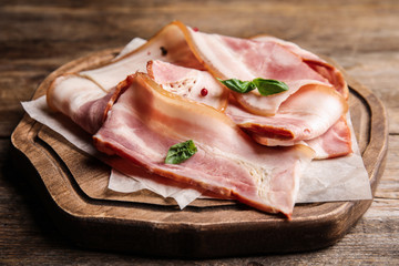 Board with slices of raw bacon on wooden table, closeup