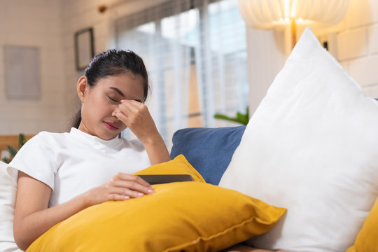 Young asian woman feeling  stress  and closed eyes  suffering from headache and lying down on sofa in living room,tired  female office worker massaging eyes,