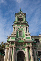 Fototapeta na wymiar The bell tower of an Orthodox church in green with a white pattern on a background of blue sky in small clouds