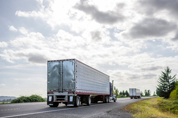 Big rig semi trucks transporting cargo in semi trailers running on the eveing local road