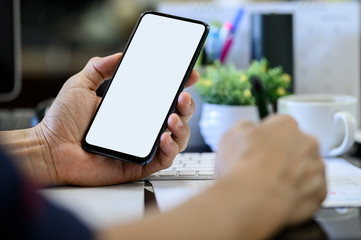 Closeup man hand holding smartphone with blank white screen while working at office desk.