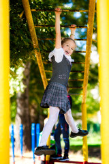 Fototapeta premium Girl schoolgirl in a school uniform climbs a sports horizontal bar