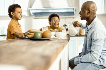 Three - two boys and man - sitting at the table, having lunch and laughing.