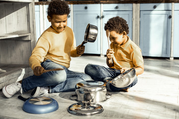 Two mischieves playing with dishes and cutlery.