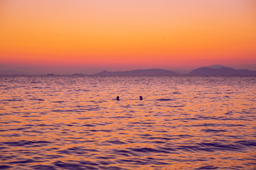 Greek Republic. Sunshine in sea and swimming people. In the distance mountains and sky. 17. Sep. 2019.