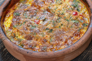 Obraz na płótnie Canvas Ceramic bowl with vegetable frittata, simple vegetarian food. Frittata with tomato, pepper, onion and cheese on wooden table, close up. Italian egg omelette
