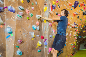 Muscular man practicing rock-climbing on a rock wall indoors