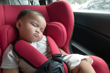 Asian baby girl on red car safety seat during trip. Parent put daughter on car seat for safety during the drive.