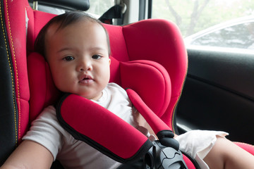 Asian baby girl on red car safety seat during trip. Parent put daughter on car seat for safety during the drive.