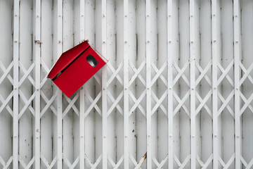 Tilted red mail box on white metal gate