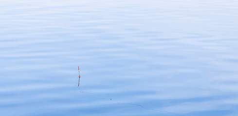 fishing life style hobby concept picture with floating fishing rod on smooth blue water surface natural background surface, empty copy space for text © Artem Kniaz