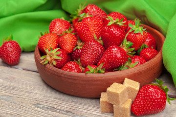 Bowl of strawberry harvest on wooden table close up